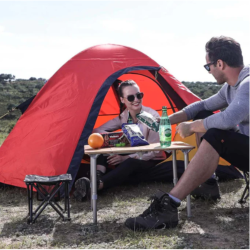 Zložljiva kamping mizica v uporabi pri kampiranju ob šotoru, primerna za piknik in kamping.