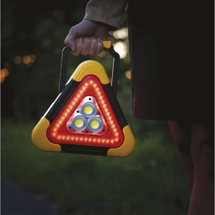  Oseba drži prižgan EMOS LED trikotnik z rdečimi in belimi lučmi za varnost v temi.