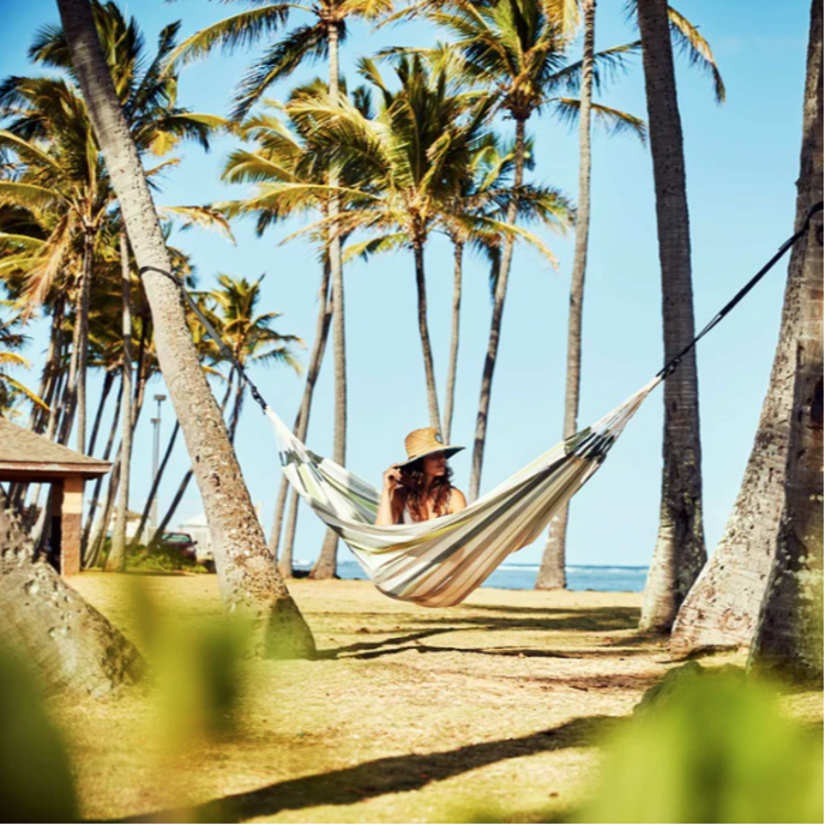 Viseča mreža v svetlih bež črtah nameščena med palmami na plaži, prikaz uporabe na prostem.