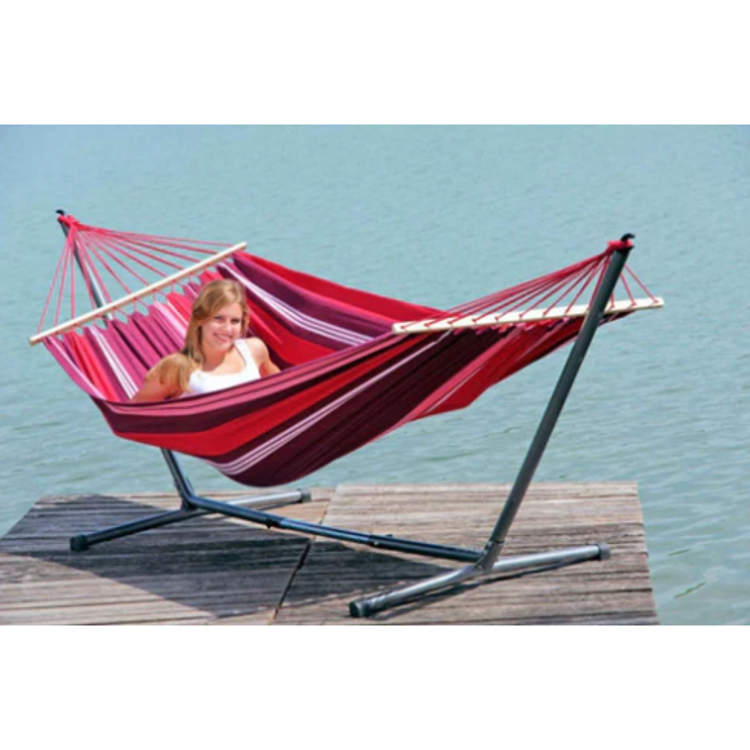 Viseča mreža na kovinskem stojalu ob vodi, rdeče‑roza barve