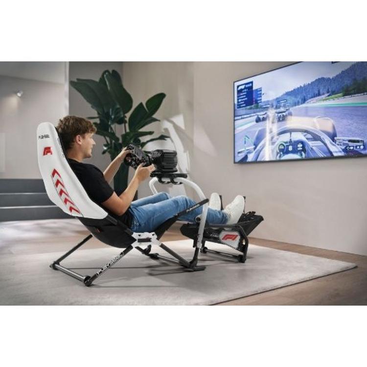 Oseba sedi v Playseat F1 simulatorju ter vozi dirkalnik na velikem zaslonu v sodobnem prostoru.