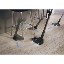 Baterijski sesalnik Hoover HF1M10H v uporabi pri sesanju trdih tal pod pohištvom z gibljivo krtačo.